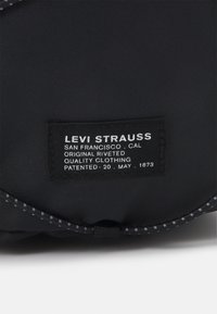 Černá látková visačka s bílým textem uvádí "Levi Strauss", "San Francisco" a "Originální nitěné kvalitní oblečení" spolu s datem patentu.