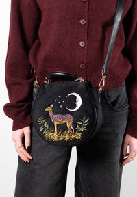 Schwarze Wildleder-Handtasche in runder Form mit aufwendiger Stickerei eines Rehs und des Mondes, verziert mit grünen und gelben Blattakzenten. Schwarzer Riemen und Griff.