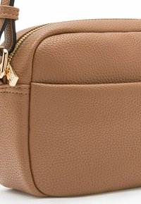 Bolso cruzado de cuero marrón claro con un acabado texturizado, cremallera dorada y herrajes pulidos. Forma rectangular compacta con un detalle de bolsillo lateral.