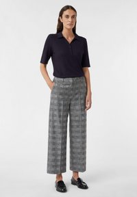 Marineblaue, gerippte Poloshirt mit kurzen Ärmeln, kombiniert mit weiten, karottenförmigen Hosen in Grautönen und schwarzen Slippern.