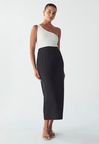Haut blanc à côtes asymétrique associé à une jupe midi noire taille haute. La tenue présente une texture lisse et une silhouette élégante.