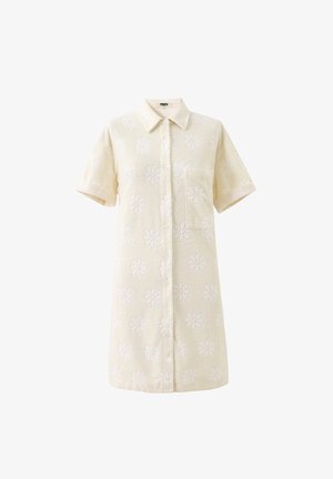 Crèmewitte jurk met korte mouwen, kraag, knopen aan de voorkant, borstzak en een subtiel textuurrijk bloemenpatroon over de hele jurk.