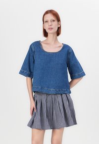 Blå denimkortärmad topp med rundad halsringning, i kombination med en veckad svart-vit rutmönstrad kjol. Enkelt design med synliga sömmar.