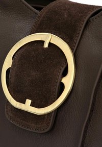 Borsa a mano in pelle marrone con una fibbia circolare in metallo dorato su una tracolla in suede marrone. Superficie texture con dettagli lucidi.