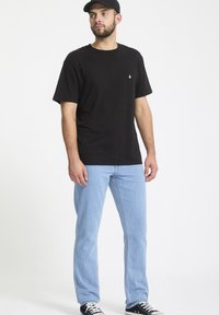 T-shirt nera in cotone con scollatura rotonda e un piccolo logo bianco; abbinata a jeans in denim blu chiaro; sneakers nere.
