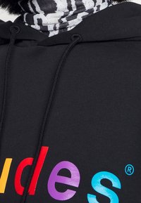 Czarny hoodie z żywym, wielokolorowym napisem. Posiada sznurki oraz miękką, teksturowaną tkaninę. Pod spodem czarna i biała wzorzysta chusta.