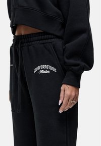 Zwarte cropped sweatshirt met lange mouwen en elastische manchetten, gecombineerd met zwarte trainingsbroeken met een geborduurd logo en een trekkoord in de taille.