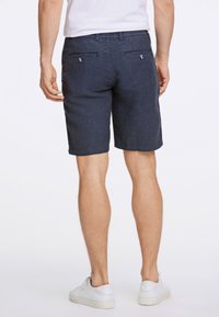 Marinblå shorts i strukturerat tyg, med två bakfickor med metallknappar och normal passform. Matchas med vita sneakers.