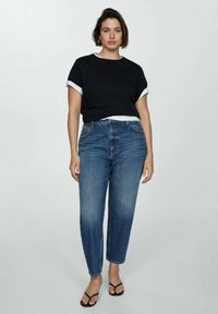 Schwarzes T-Shirt mit kurzen Ärmeln und weißen Akzenten, kombiniert mit hoch taillierten blauen Jeans. Sandalen mit dünnen Riemen runden das Outfit ab.