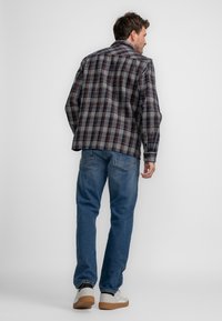 Geruit overhemd in navy, grijs en roesttinten, met een relaxte pasvorm en lange mouwen. Gecombineerd met blauwe jeans en lichte sneakers.