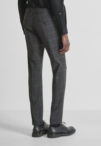 Pantalones de vestir a cuadros grises con un corte entallado, frente plano y dos bolsillos traseros. Combinados con zapatos negros y cortados para un acabado limpio.