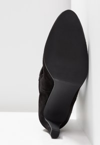 Botte noire à bout pointu et talon fin, vue du côté de la semelle, avec une prise texturée et un talon haut et élégant.