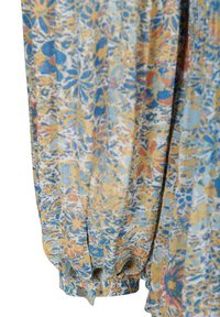 Manche longue avec poignet élastique et bouton, avec un motif floral en bleu, jaune et orange sur un tissu clair.