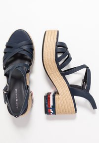 Tyrkysové platformové sandály s křížovými pásky, espadrilový styl tkané mezipodešve a ozdobným vícestupňovým vzorem na podpatku.