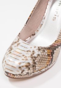 Gros plan d'une chaussure à talon pour femme avec un motif en peau de serpent brillante aux tons beige, marron et orange clair.