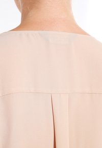 Blusa color pesca realizzata in tessuto morbido e leggero. Presenta una piega sul retro e un design del collo discreto.