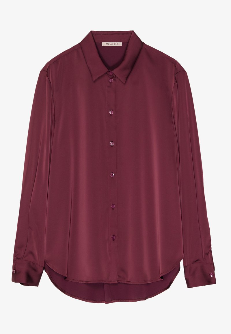 Blusa bordeaux a maniche lunghe in morbida satin, con colletto, chiusura a bottoni davanti e orlo arrotondato. I bottoni si abbinano al colore del tessuto.