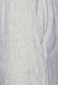 Ljusblått, texturerat tyg med ett subtilt mönster, med synliga sömmar längs kanterna och en avslappnad form.