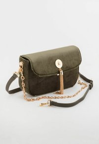 Zielona zamszowa torebka z klapą, złotymi łańcuszkami i dekoracyjnym frędzlem. Posiada odpinany pasek do uniwersalnego noszenia.