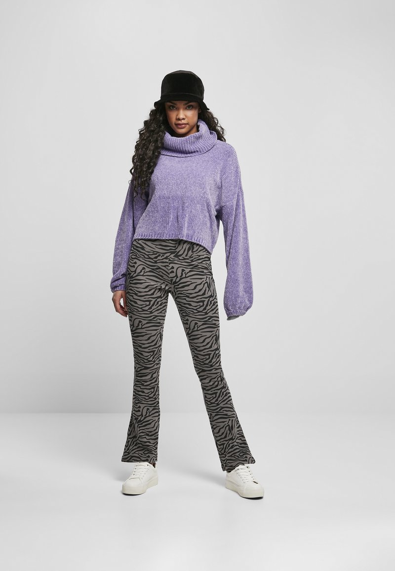 Pull court violet avec col roulé, associé à un pantalon évasé à imprimé zèbre noir et gris, et des baskets blanches. Chapeau seau noir.