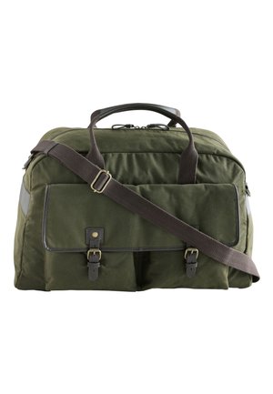 Groene canvas reistas met twee voorvakjes met gespen, dubbele handvatten en een verstelbare bruine schouderband tegen een witte achtergrond.