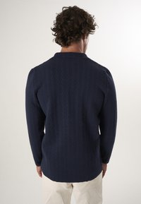 Marineblauw overhemd met lange mouwen, een gestructureerd visgraatpatroon, knopenkraag en rechte snit, gecombineerd met lichtgekleurde broeken.