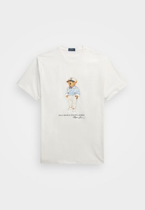 Biała koszulka z krótkim rękawem z grafiką misia w czapce, niebieskiej koszuli, szelkach i kremowych spodniach oraz napisem "Polo Bear by Ralph Lauren".