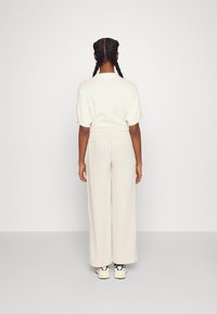 Top beige de manga corta combinado con pantalones de pierna ancha de un tono beige claro. El conjunto cuenta con una cinturilla elástica y una textura suave. Zapatillas deportivas con acentos coloridos.