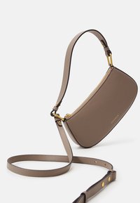 Eine gebogene, braune Ledertasche für die Schulter mit einem goldenen Reißverschluss, verstellbarem Trageriemen und eingeprägtem Logo. Glatte Oberfläche mit minimalistischem Design.