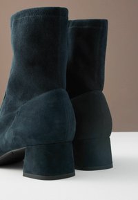 Mörk teal mockaskinn ankle boots med en jämn textur, med en blockklack och sydda sömmar, som visar en modern design och silhuett.