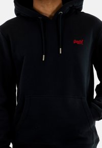Sudadera azul marino con capucha regulable y bolsillo tipo canguro. Presenta un pequeño logotipo rojo en la parte izquierda del pecho. Fabricada con tela suave.