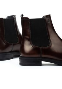 Botas Chelsea de cuero marrón con paneles laterales elásticos negros, acabado suave, punta redondeada y un tacón bajo negro; tirador en la parte trasera.