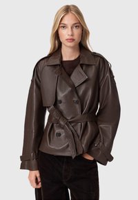 Bruine leren dubbelknopen jas met riem, brede revers en oversized mouwen. Gladde textuur en subtiele glans.