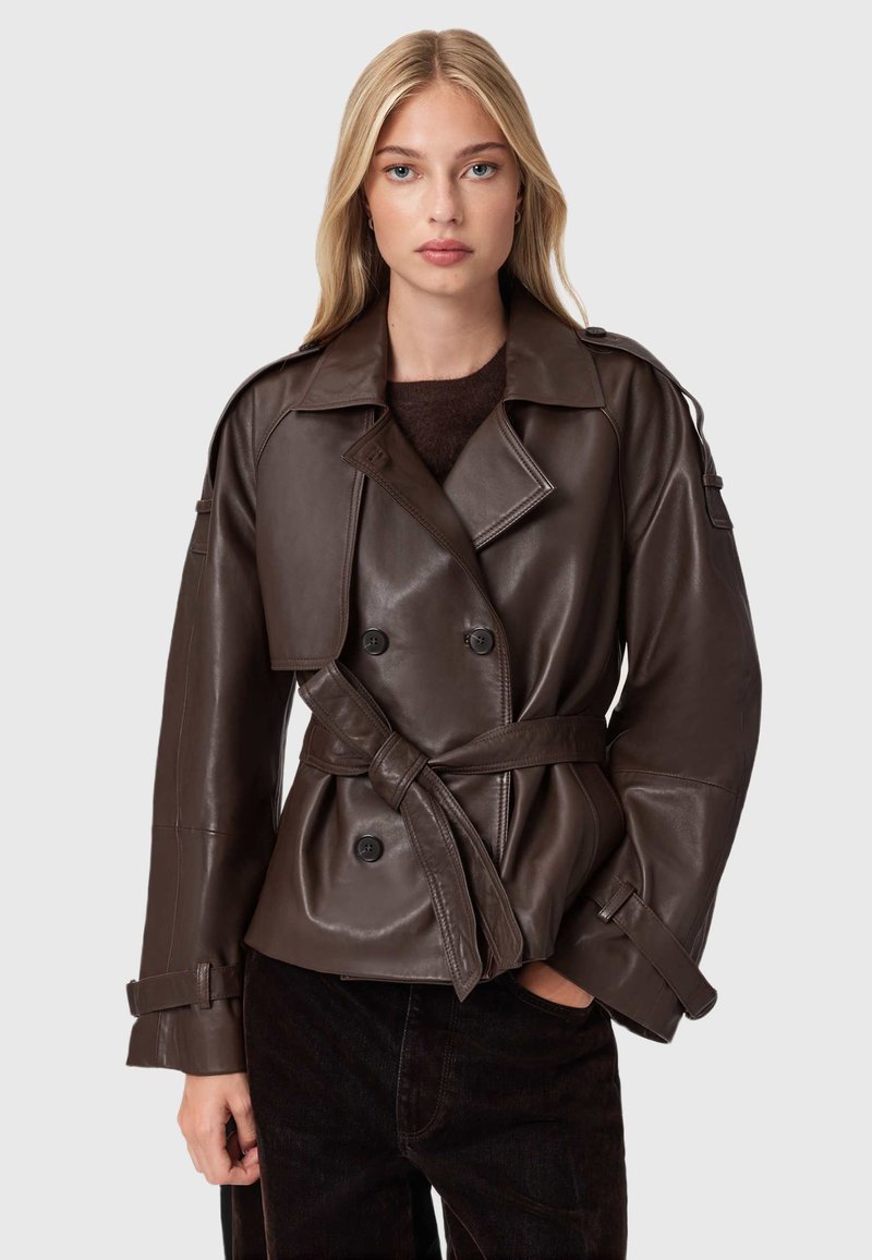 Bruine leren dubbelknopen jas met riem, brede revers en oversized mouwen. Gladde textuur en subtiele glans.