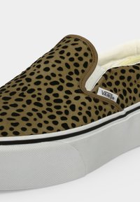 Baskets slip-on avec motif tacheté marron et noir, semelle blanche avec bande noire, et étiquette logo Vans sur le côté.