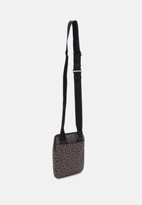 Borsa di tessuto marrone con un motivo geometrico, chiusura con zip e una lunga tracolla nera regolabile per un uso crossbody.