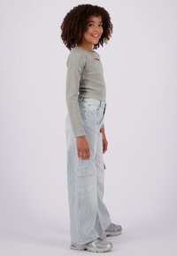 Maglietta grigia a maniche lunghe con dettagli cut-out; pantaloni cargo a righe blu chiaro con gamba larga; sneakers argentate con superficie testurizzata; vista di profilo.