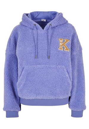 Lila bolyhos kapucnis pulóver, zsinóros kapucnival, elülső zsebbel és struktúrált felülettel. Arany és krém színű hímzett "K" betűvel díszítve.