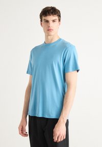 Hellblaues T-Shirt mit kurzen Ärmeln aus weicher Baumwolle, mit klassischem Rundhalsausschnitt und lockerer Passform. Minimalistisches Logo-Detail auf der Brust.
