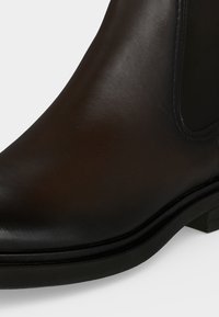 Gros plan d'une botte Chelsea en cuir noir avec panneau latéral élastique et petit talon sur fond blanc.
