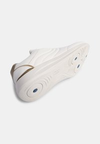Fehér sneaker sima bőrből készült felsőrésszel, texturált talppal és arany árnyalattal a saroknál. Áramvonalas dizájnnal és kör alakú mintázattal ellátott talppal rendelkezik.