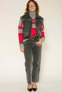 Veste en denim avec détails cloutés portée sur un pull rayé multicolore rose, gris et marron. Jean noir taille haute à jambes droites et talons.
