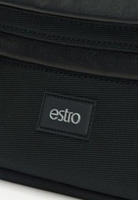 Czarna torba na ramię z połączenia gładkiej skóry i fakturowanej tkaniny, z wytłoczonym logo "estro" na prostokątnej łatce.