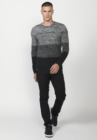Pulover tricotat gri închis și negru cu o textură contrastantă, având un guler rotund și mâneci lungi ajustate. Purtați cu pantaloni și pantofi negri.