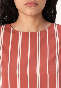 Terracotta-bluse med lodrette hvide striber, lavet af et blødt, glat stof med rund halsudskæring og minimalistisk design.