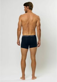 Tengerészsötét kék boxer alsónemű fehér derékszíjjal, amelyen a "U.S. Polo Assn." logó található. Szűk szabás, sima anyag és rövidített fazon jellemzi.
