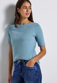 Lichtblauw kortærmet top in een zachte stof met een bootnek. Draag het met donkerblauwe jeans met een klassiek vijf-pocketontwerp.