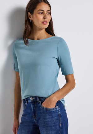 Haut bleu clair à manches courtes en tissu doux avec un col bateau. Porté avec un jean bleu foncé au design classique à cinq poches.