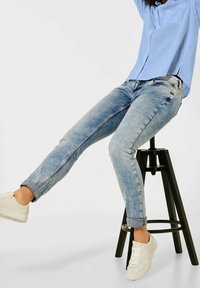 Světlé modré džíny s úzkým střihem, s ohrnutými manžetami, kontrastním prošitím a zadními kapsami, doplněné o bílé tenisky.