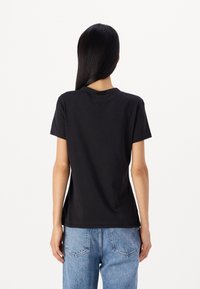 T-shirt nera a maniche corte con scollatura tonda, realizzata in morbido cotone, abbinata a jeans di denim a vita alta azzurri. Design semplice e vestibilità comoda.